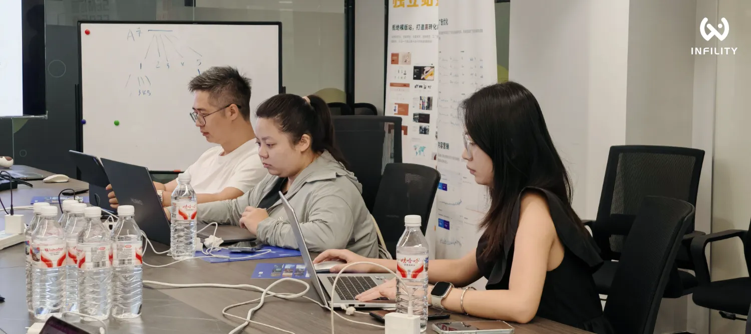 办公室会议场景中，三名员工坐在长桌前专注操作电脑，桌上摆放多瓶水，背景有白板和海报。
