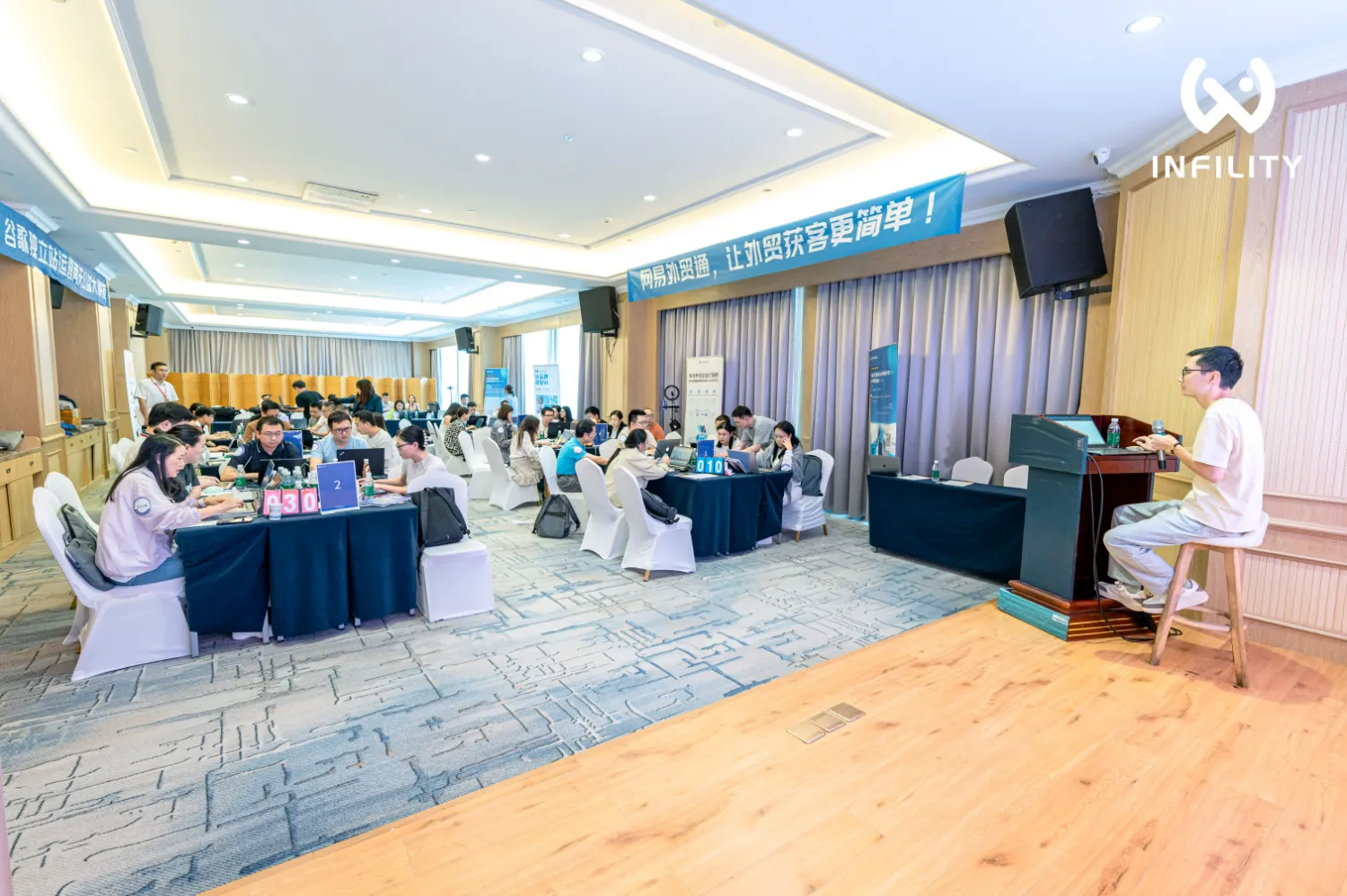 众多参会者正使用笔记本电脑进行实操，前方讲师正在讲解，背景悬挂网易外贸通及谷歌独立站运营大赛宣传横幅。