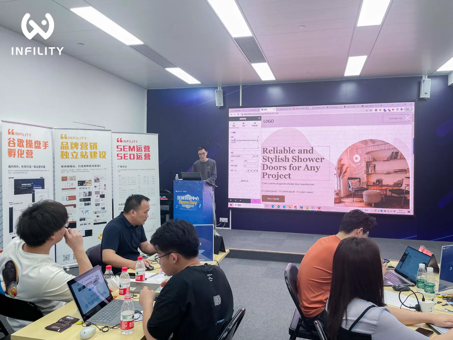 讲师在INFINITY谷歌操盘手孵化营现场演示独立站网页设计，背景展板涵盖品牌营销、SEM与SEO运营内容，学员专注听讲。