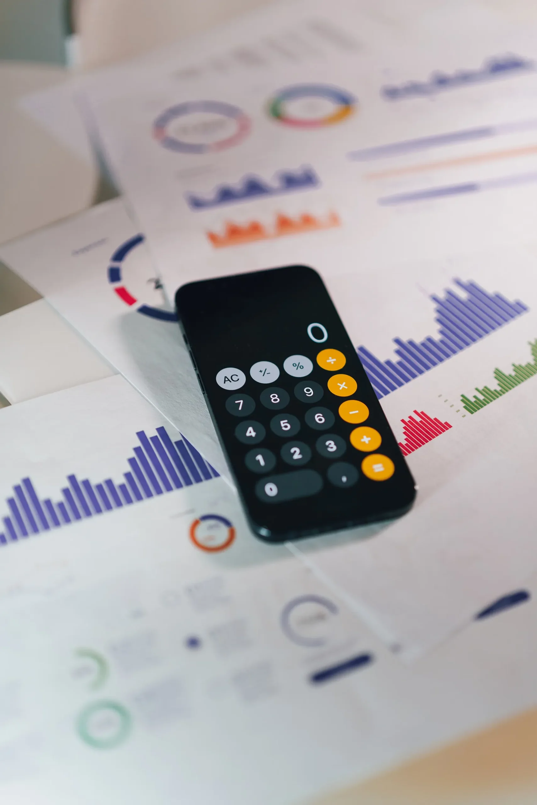 A smartphone calculator resting on printed charts and bar graphs illustrating campaign performance and cost metrics, representing Infility’s data-driven Google Ads budgeting and ROI modeling. This visual connects directly to Infility’s 批量导入类目: 预算与成本评估 service for B2B export websites and SEM cost optimization.